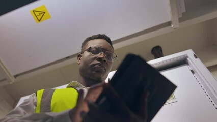 Poster - Engineering, digital tablet and male electrician doing maintenance or repair on technical system. Technology, control room and professional black man industry worker technician working on switchboard