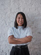 © Make_story Studio - Portrait of a smiling asian businesswoman standing with arms folded and looking at camera isolated over grey background