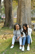 © Prathankarnpap - Happy senior mother and adult daughter using smart phone while sitting on green grass against calm nature park