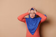 Unhealthy Middle-Eastern Muslim woman in blue hijab, rubbing temples to cure headache problem, suffering from tension, migaine stress, grimacing in pain, high blood pressure, isolated beige background