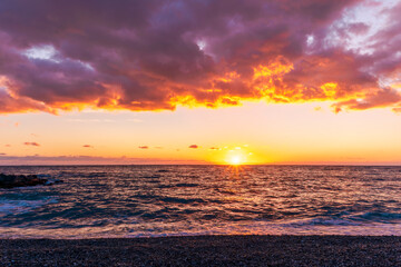 empty beach with surf during beautiful sunrise or sunset with surf, clouds and golden sun