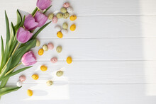 Chocolate Colorful Decorative Eggs And Pink Tulips On A White Wooden Table On Grey Background. Happy Easter. Front View