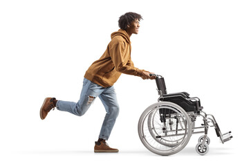 Wall Mural - Full length profile shot of a young african american man running and pushing an empty wheelchair