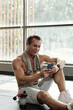 © DragonImages - Sportsman sitting on gym floor and choosing music for training from playlist on smartphone