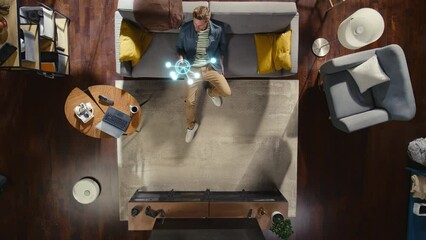 Top View Of Caucasian Man In the Loft Apartment Sitting Down on The Couch and Connecting Smartphone to Convenient Smart Home System. VFX Animation Visualizing Connected Devices. Laptop, TV, Speaker.