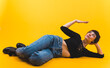 © PoppyPix - Full shot. Woman lying on her side in jeans and a black top, with one bent arm raised. High quality photo