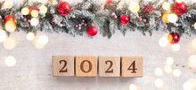 Christmas Background With Red Baubles Hanging On Pine Tree. Banner With The Number 2024 On Wooden Cubes