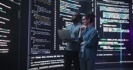 Fototapete - Portrait Two Diverse Developpers Using Laptop Computer, Discussing Lines of Code that Appear on Big Screens Surrounding Them. Male and Female Programmers Creating a Software Together, Fixing Bugs