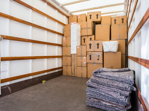the inside of a removal van, showing fabric blankets stacked and a background of cardboard boxes. co