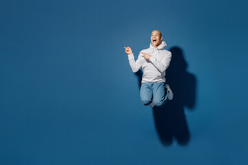 Wall Mural - Full body young fun happy man of African American ethnicity wearing white hoody jump high point index finger aside on workspace area isolated on plain dark royal navy blue background studio portrait.