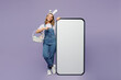 Full body young woman wear casual clothes bunny rabbit ears point index finger indicate on big huge blank screen mobile cell phone with area isolated on plain purple background. Happy Easter concept.