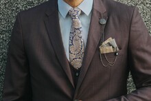 Man In A Brown Suit, White Striped Shirt With Paisley Tie And A Lapel Chain Jewelry