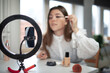 beauty blogging, technology and people concept portrait of a happy smiling girl blogger with ring light and smartphone applying make up at home. making a influencer video