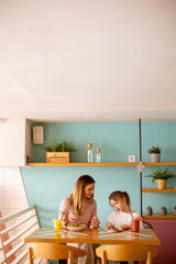 Wall Mural - Mother and daughter having a breakfast with fresh squeezed juices in the cafe