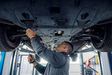 An Auto Mechanic Is Repairing Car While Standing Under It At Mechanic's Shop.