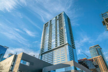 Modern High-rise Condominium With Balconies In A Low Angle View At Austin, Texas. Residential Building In The Middle Of Modern Office Buildings Against The Blue Sky.