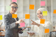 © David - Young Asian woman Creative team use post it notes to share idea sticky note on glass wall. Asian business people design planning and Brainstorming thinking sticky History notes concept.
