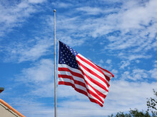USA National Flag Waving Lowered To Half Mast On Wind Against Blue Sky. American Stars And Stripes Spangled Banner As Symbol Of Democracy