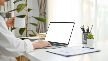 Cropped image of professional Asian businesswoman sipping coffee and using laptop at her desk