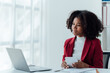 © Tj - happy young businesswoman African American siting on the chiar cheerful demeanor raise holding coffee cup smiling looking laptop screen.Making opportunities female working successful in the office.