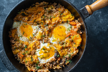 Wall Mural - Boiled rice with fried eggs, pumpkin, peppers, carrots and onions in a cast iron pan, closeup. Food background. Healthy food