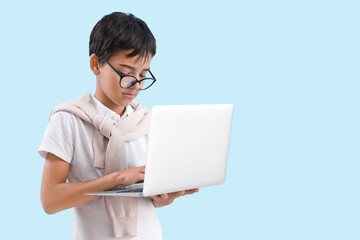 Wall Mural - Little boy in eyeglasses using laptop on blue background