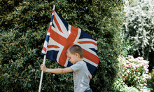 Side View Of Boy Holding British Flag While Standing By Plants At Park