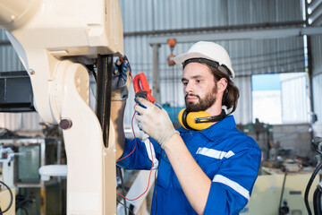 Wall Mural - Male electrician worker checking, repair, maintenance operation electric system of robotic arm in factory. Male electrician using electrical meters working with operation electric system of robot arm