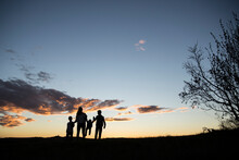 Happy Silhouette Family Standing On Field Against Sky During Sunset