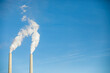 © Cavan Images - Low angle view of smoke emitting from chimneys against blue sky