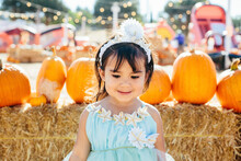 Cute Smiling Girl In Dress Looking Down While Standing Against Pumpkins During Halloween