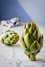 Two Fresh Artichokes On A Marble Counter