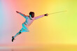 Long attack. Young man, male fencer with sword practicing in fencing over gradient pink-yellow background in neon light. Sportsman shows fencing technique