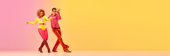 Stylish expressive excited couple of professional dancers in retro style clothes dancing disco dance over pink-yellow background. Concept of 70s, 80s fashion style, music and emotions