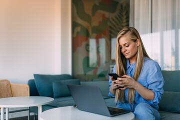 Photo of a smiling woman, using a mobile phone while working at the office.