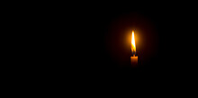 A Single Burning Candle Flame Or Light Glowing On An Orange Candle On Black Or Dark Background On Table In Church For Christmas, Funeral Or Memorial Service With Copy Space