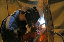 A Worker Welding Metal Parts On A Construction Site. A Welder Welds Parts Of A Large Machine In A Metallurgical Workshop. An Interesting Example Of Manual Work.	