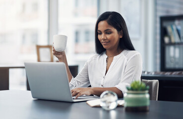 Poster - Fuelled with ambition. Shot of a young businesswoman drinking coffee while working on a laptop in an office.