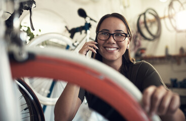 Wall Mural - Just calling to confirm we received your bike. Shot of an attractive young woman crouching down in her bicycle shop and using her cellphone.