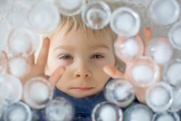 Wall Mural - Portrait of blond toddler boy, lying under ice cubes, looking at camera