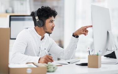 Poster - I better read through this carefully. Shot of a young businessman wearing headphones while working on a computer in an office.