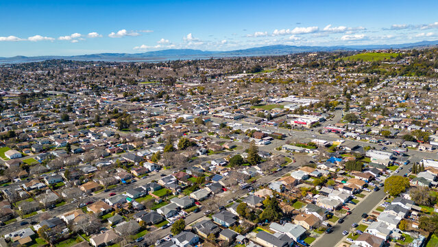 aerial photos over a community in vallejo, california with houses, streets, cars and parks on a sunn