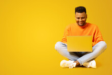 Serene Indian Male Student Is Using Laptop For Online Studying Sitting On The Floor Isolated On Yellow, Preparing Homework, Researching Topic, Positive Hindu Guy Typing, Copy Space