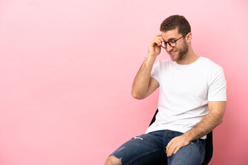 Poster - Young man sitting on a chair over isolated pink background laughing