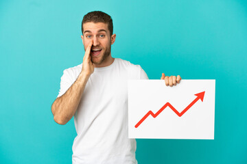 Wall Mural - Handsome blonde man over isolated blue background holding a sign with a growing statistics arrow symbol and shouting