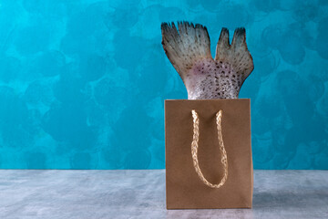 Rainbow trout tail with fin in a paper gift bag against the blue background. Seafood delivery concept