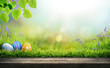 canvas print picture - Three painted easter eggs celebrating a Happy Easter on a spring day with a green grass meadow, bright sunlight, tree leaves and a background with copy space and a wooden bench to display products.