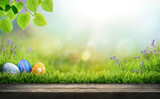 Fototapeta  - Three painted easter eggs celebrating a Happy Easter on a spring day with a green grass meadow, bright sunlight, tree leaves and a background with copy space and a wooden bench to display products.