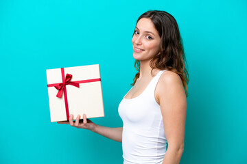 Wall Mural - Young caucasian woman holding a gift isolated on blue background smiling a lot