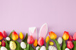 Easter concept. Top view photo of rabbit bunny ears colorful easter eggs and tulips flowers on isolated lilac background with empty space